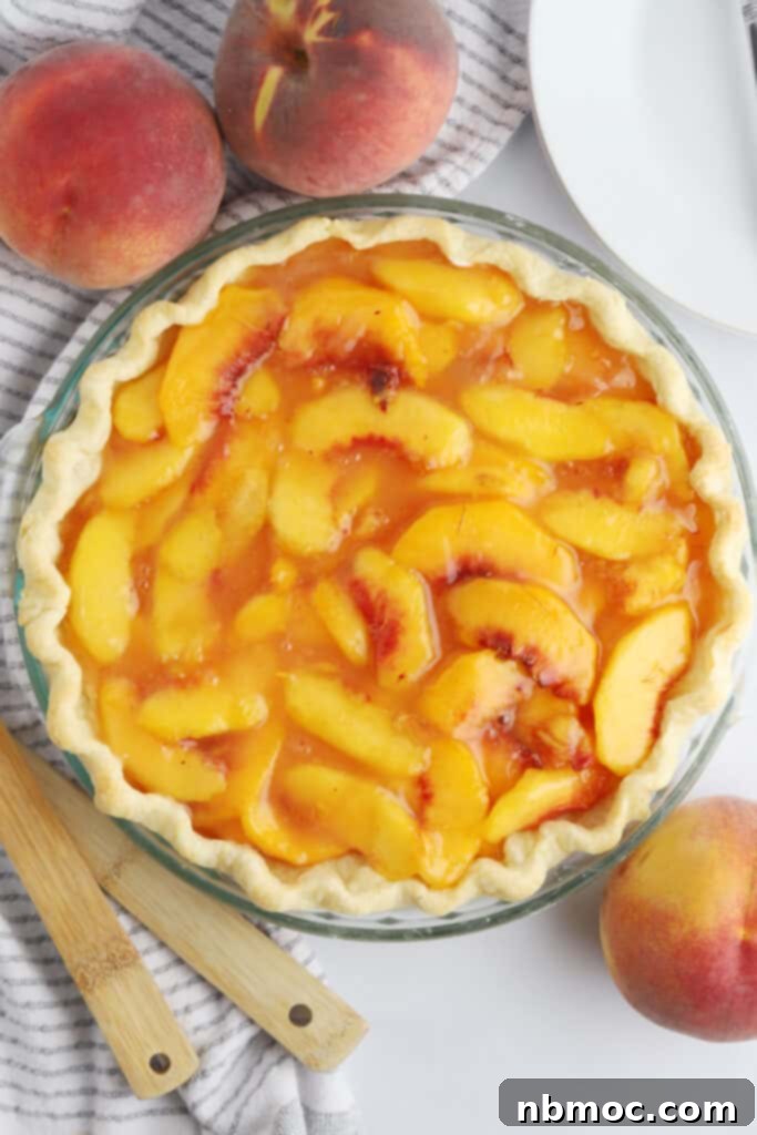 A fresh peach pie inside a fluted pie crust on a tabletop.