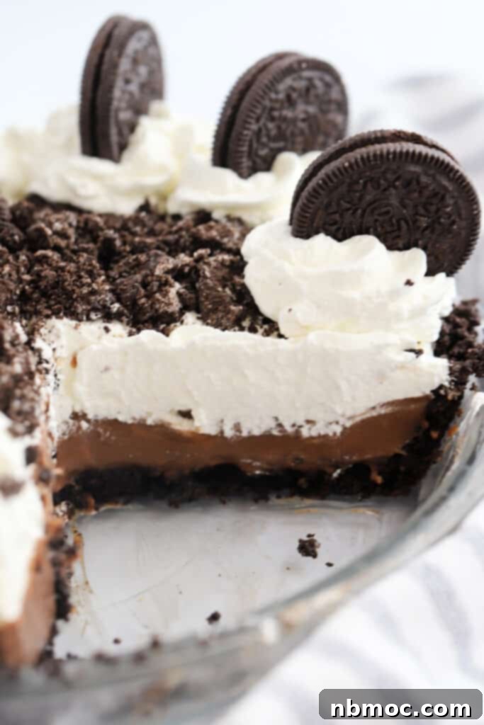 Velvety Chocolate Indulgence 2 Oreo pudding pie in a pie plate with a slice removed, topped with whipped cream and Oreo cookies.