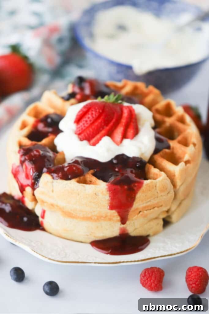 A plate with a waffle covered in berry syrup and whipped cream, invitingly presented.