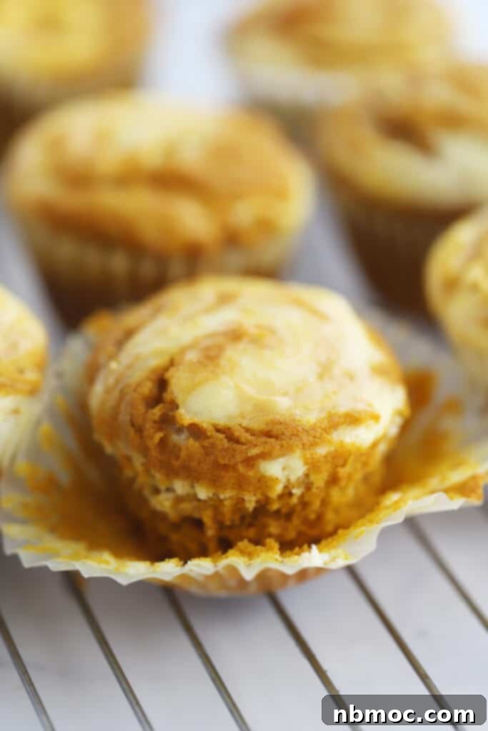 A wire rack full of freshly baked pumpkin cheesecake muffins, golden brown with visible cream cheese swirls.