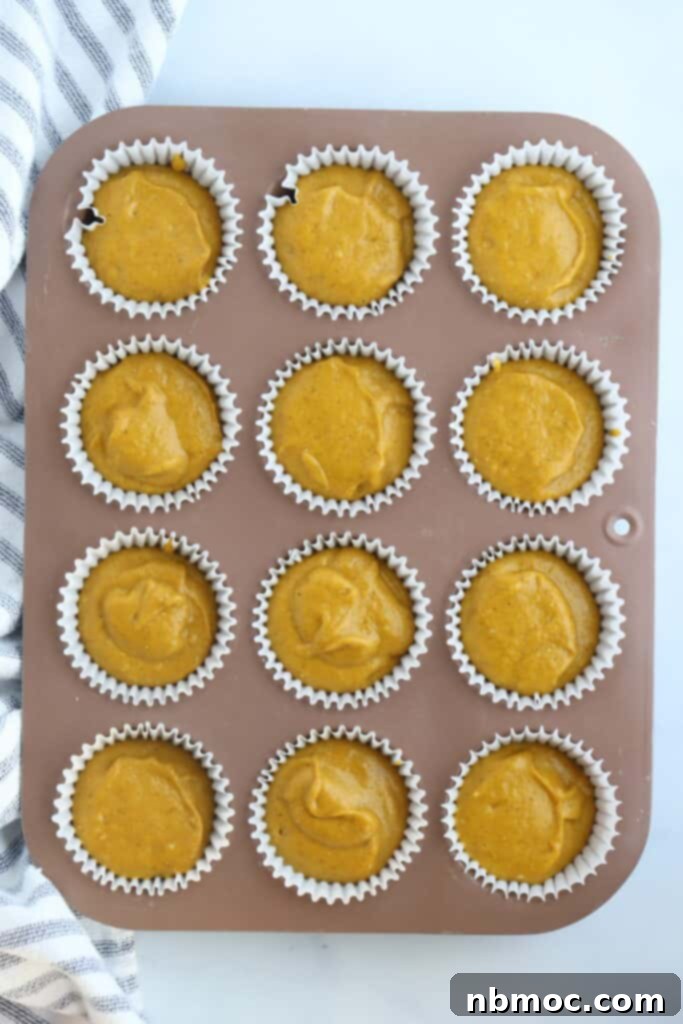 A muffin pan filled with pumpkin muffin batter and streusel, ready to bake.