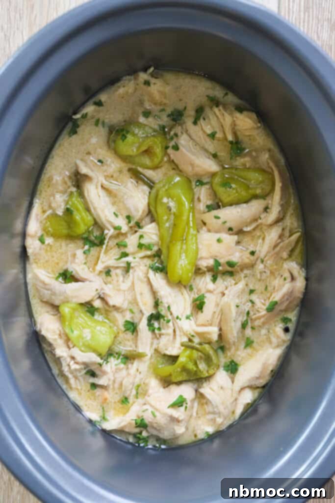 A slow cooker filled with shredded chicken and pepperoncini for making this mississippi chicken crock pot recipe. Tender, juicy, and flavorful chicken is ready to be served.