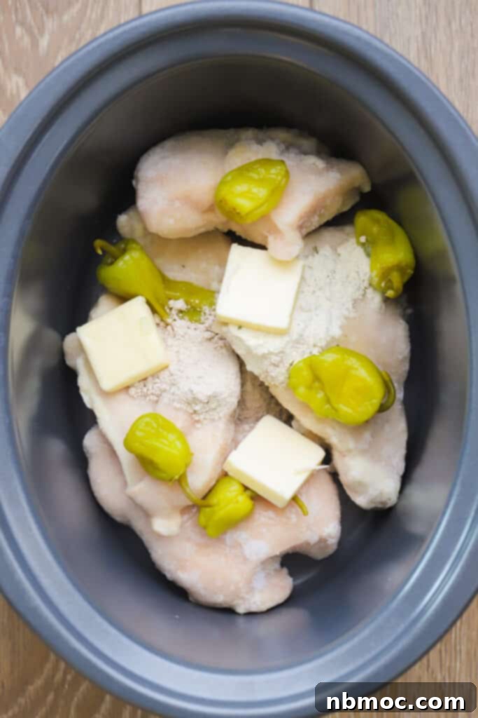 Chicken breasts, pepperoncini, butter and spice mix in the bottom of a crock pot ready to cook. The ingredients are perfectly layered for optimal slow cooking.