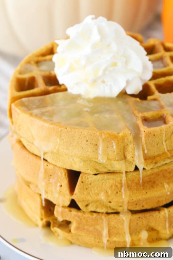 A stack of pumpkin spice waffles topped with syrup and whipped cream. 