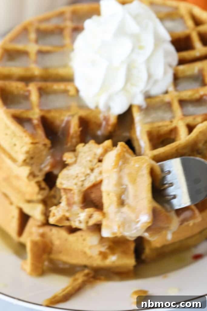 A fork digging into a stack of waffles topped with whipped cream.