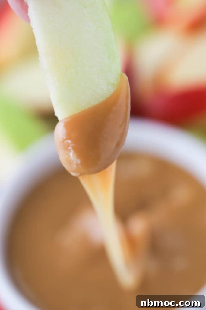 A close-up shot of a single, vibrant red apple slice generously coated in thick, golden caramel dipping sauce, ready to be enjoyed.