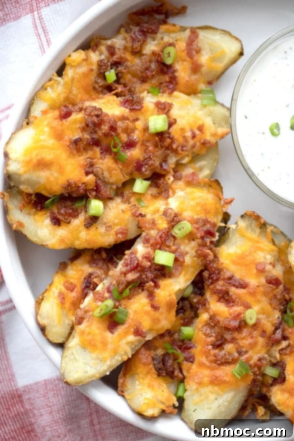Loaded baked potato skins on a serving dish, topped with sliced green onions. recipe for loaded potato skins. 