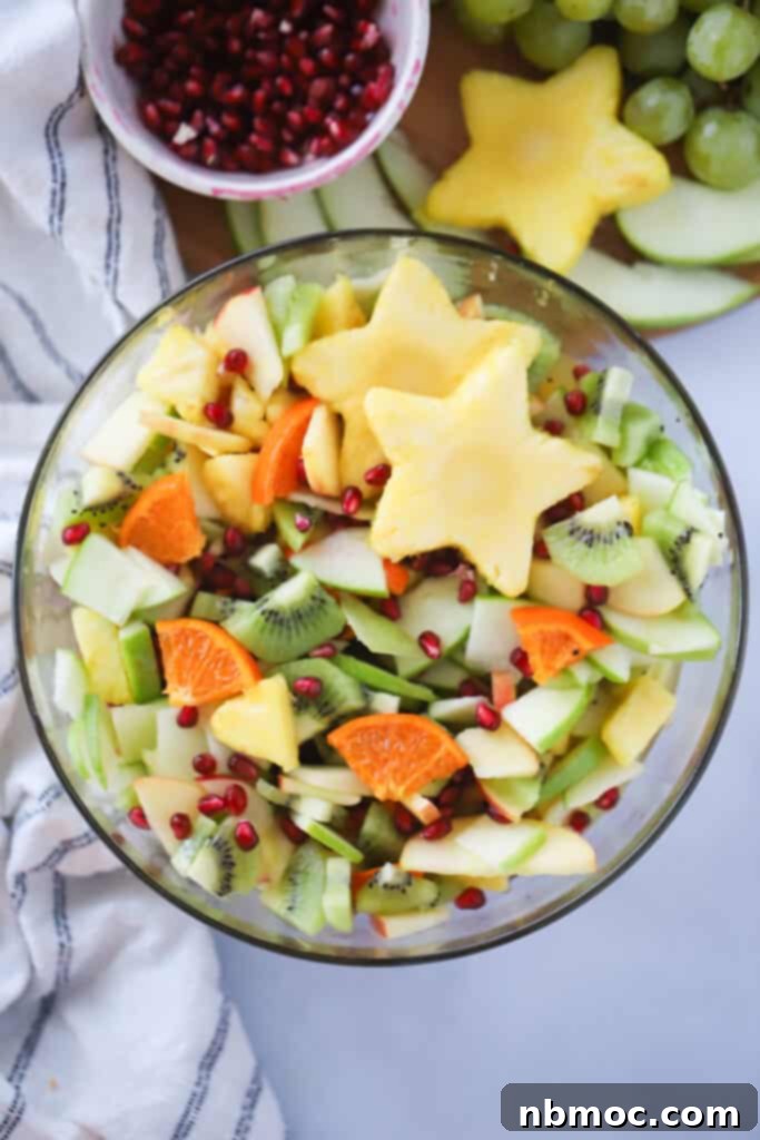 A large glass serving bowl full of winter fruit salads on a table next to a small bowl full of pomegranate seeds. 
