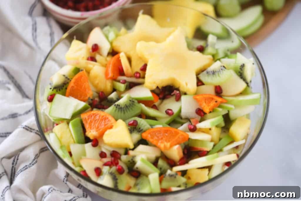 A large bowl full of fruit salad in winter, with pineapples cut in the shape of stars, kiwi, apples, and citrus.