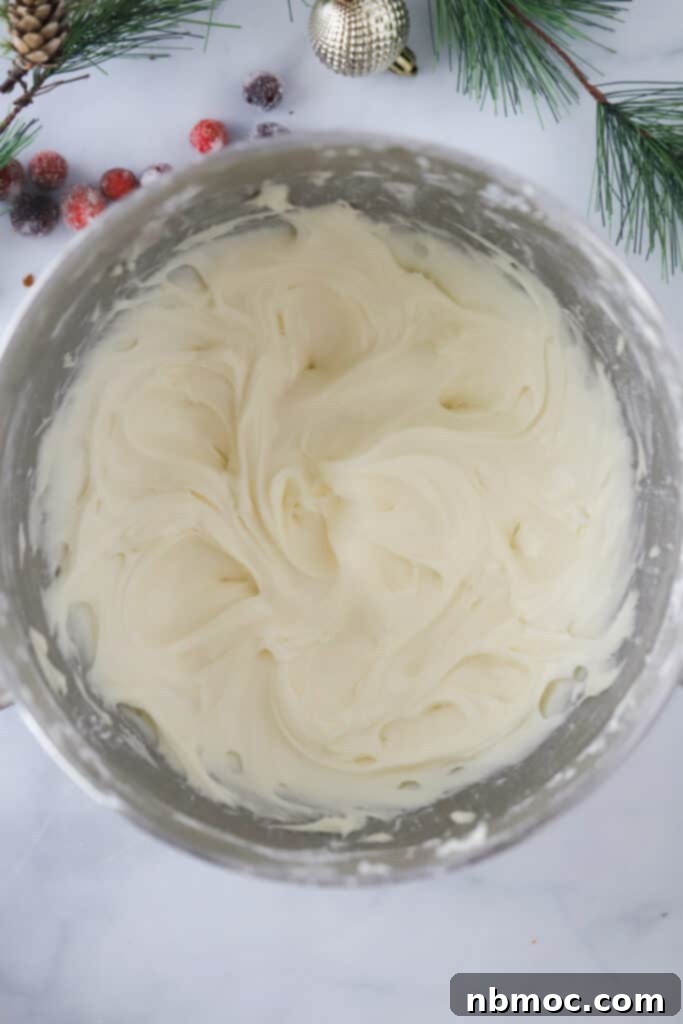 A large stainless steel mixing bowl filled with creamy, white cream cheese frosting, perfectly whipped and ready to be spread onto freshly baked cinnamon rolls for the ultimate indulgence.