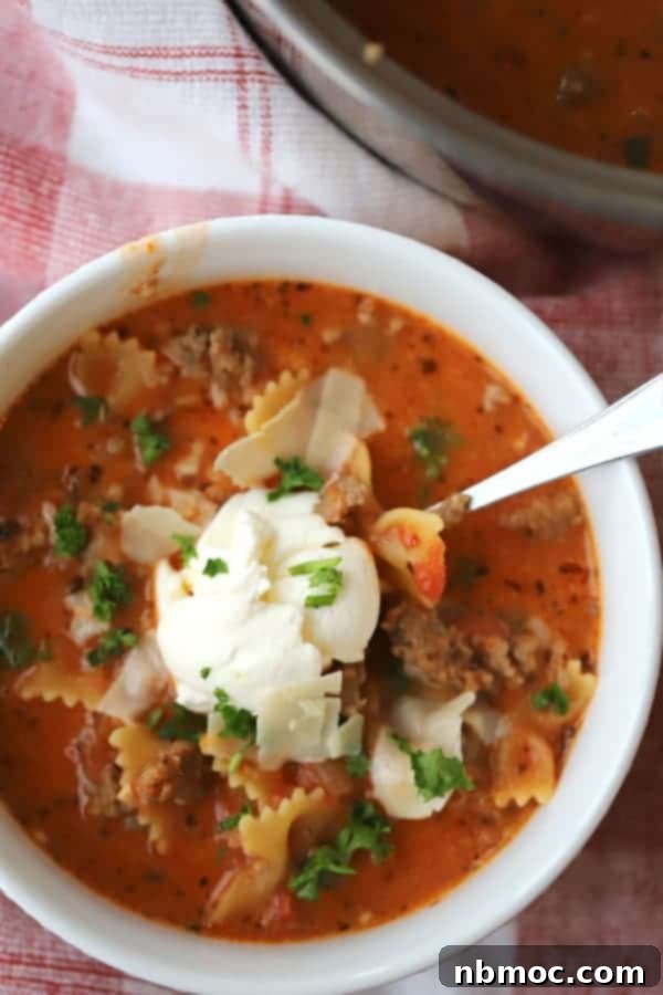 Lazy lasagna soup in a bowl, generously topped with creamy ricotta cheese, grated Parmesan, and fresh parsley for garnish.