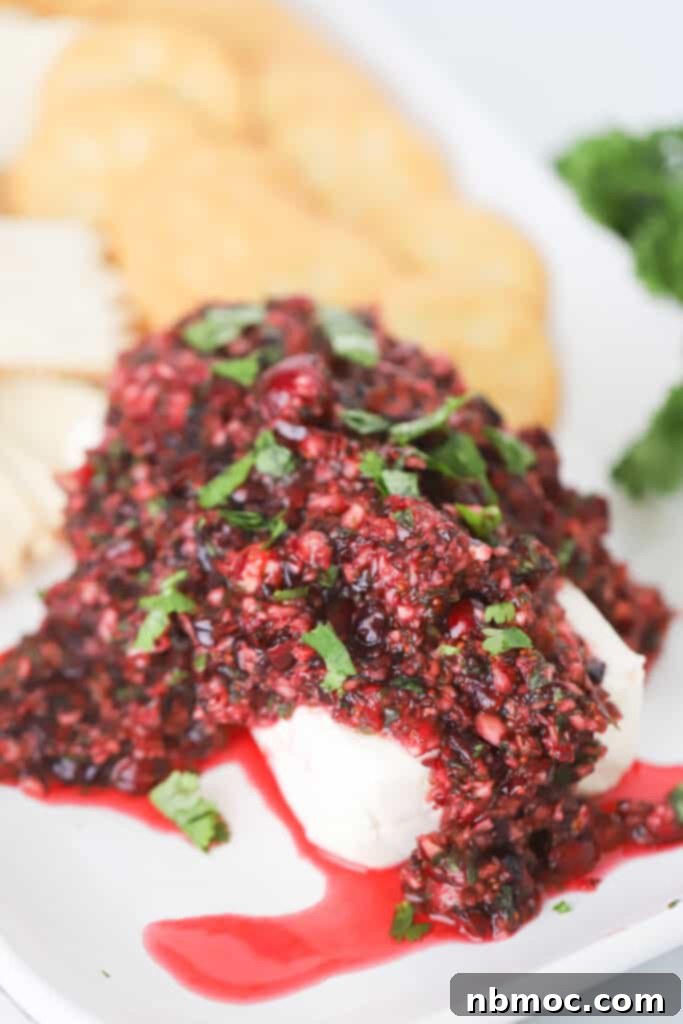 A serving platter with cranberry jalapeno salsa piled on top of a brick of cream cheese.