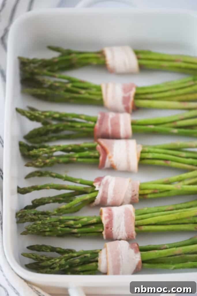 Crispy Bacon Asparagus Bundles 5 Bacon Wrapped Asparagus oven baked. Asparagus bundles wrapped in slices of bacon in a baking dish.