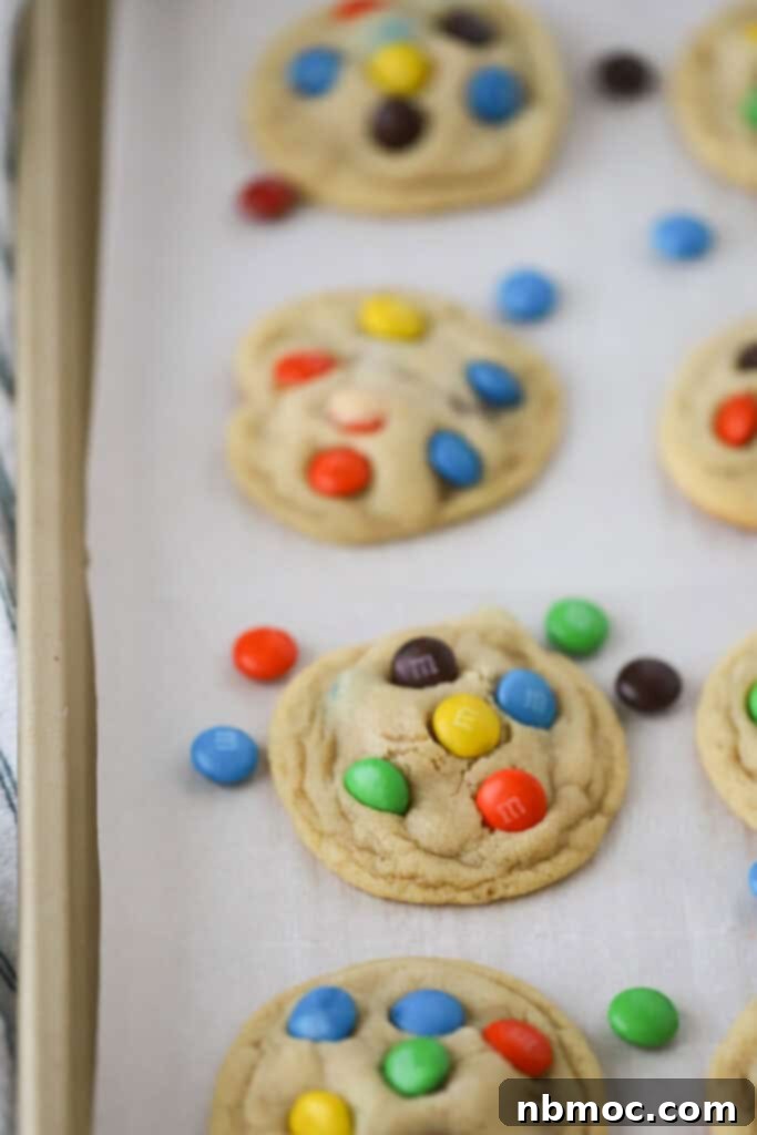 A close-up of warm, homemade M&M cookies cooling on a wire rack after baking, showing their soft centers.