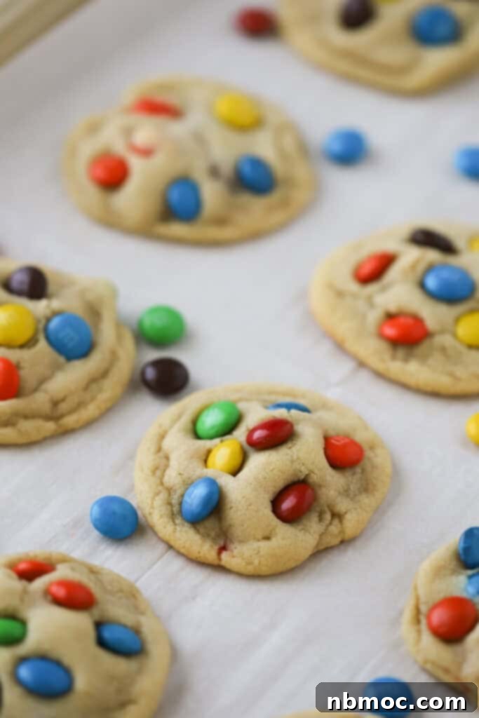 Freshly baked chocolate M&M cookies with melted candy shells on a baking sheet, ready for cooling.