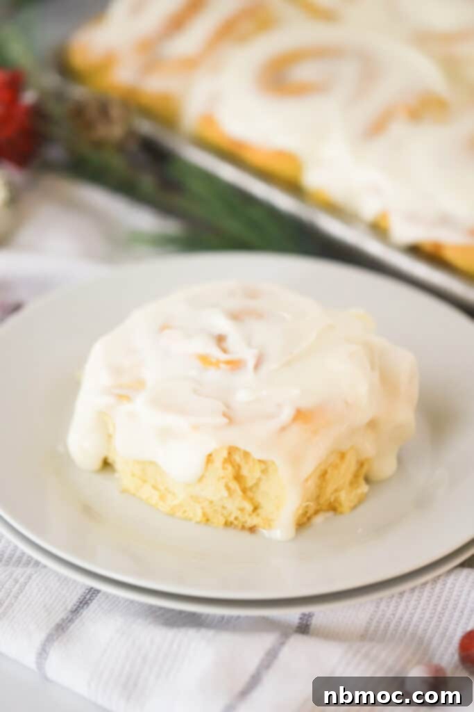 A close-up shot of a single frosted pumpkin cinnamon roll on a white plate, highlighting the creamy icing and soft dough.