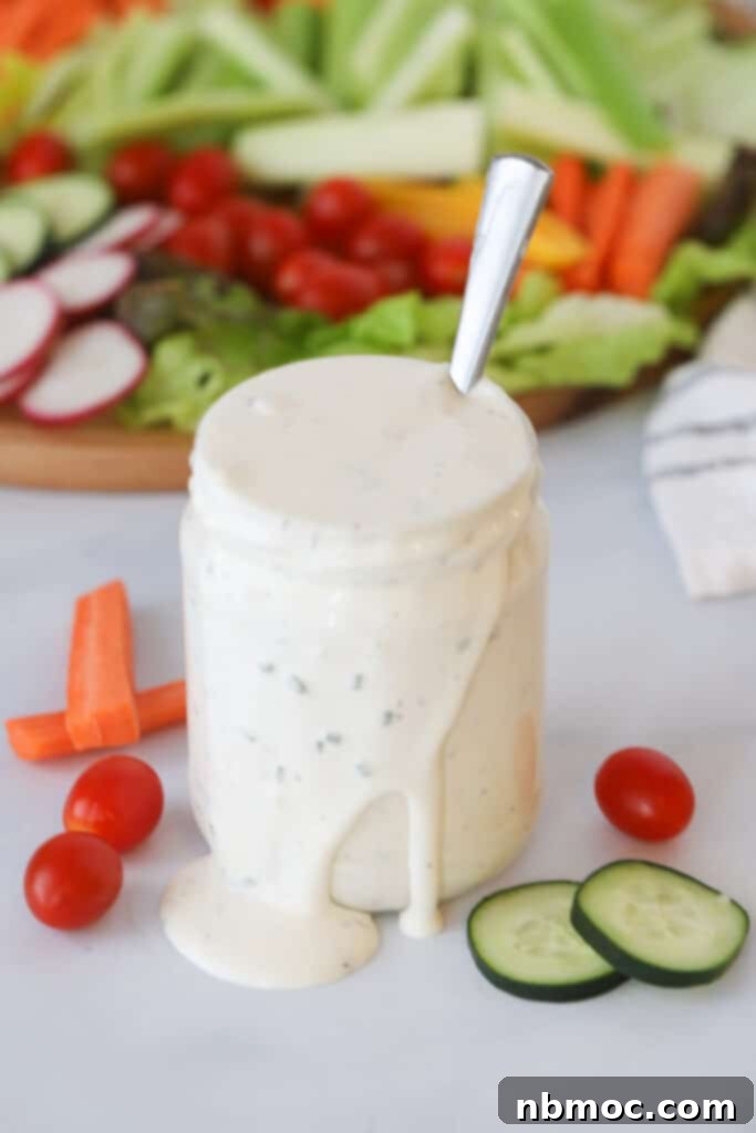 A glass jar overflowing with creamy homemade buttermilk ranch dressing, set against a backdrop of a colorful platter of fresh vegetables, ready for dipping. This ranch salad dressing recipe is a game-changer for any meal.