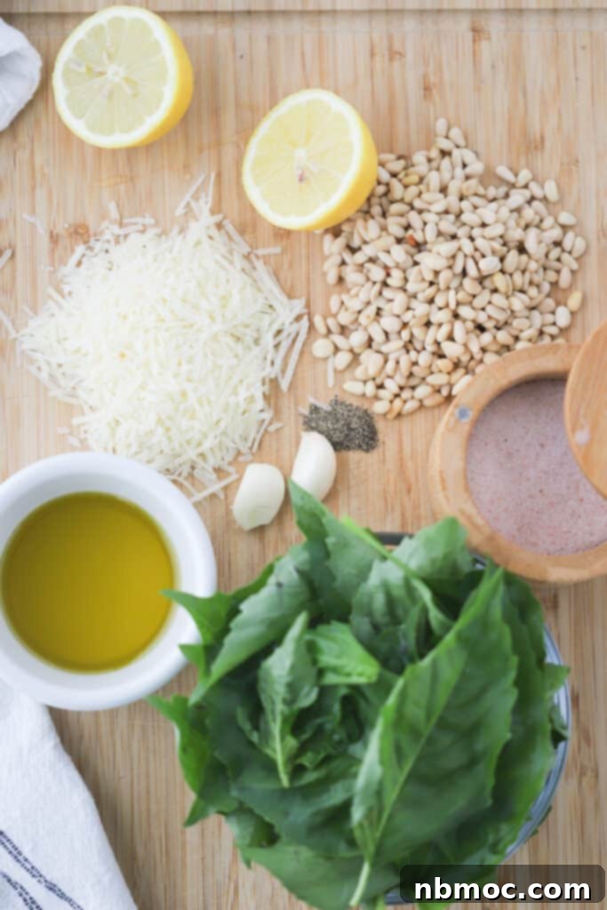 Pine nuts, cheese, lemons, fresh basil, olive oil, salt and garlic on a cutting board, ready to make one of the best homemade pesto recipes.