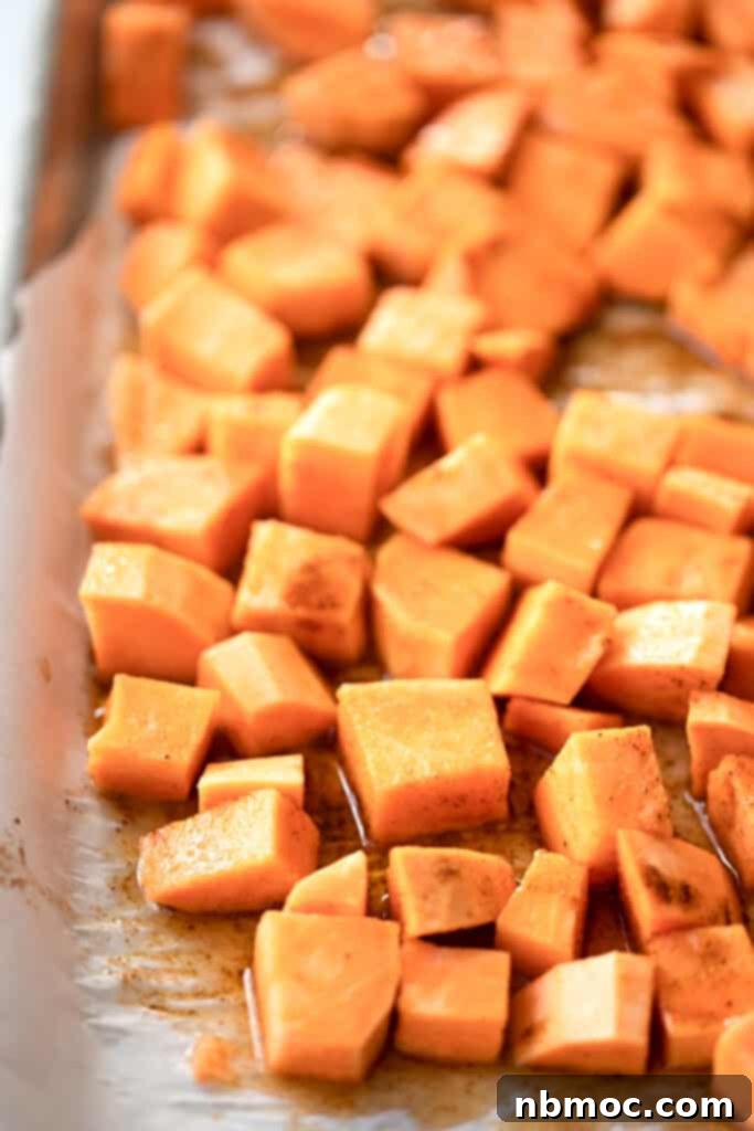 Smoky Chili Sweet Potato Cubes 3 baked sweet potato cubes on a baking sheet, with a sweet potato spice mix coating them.