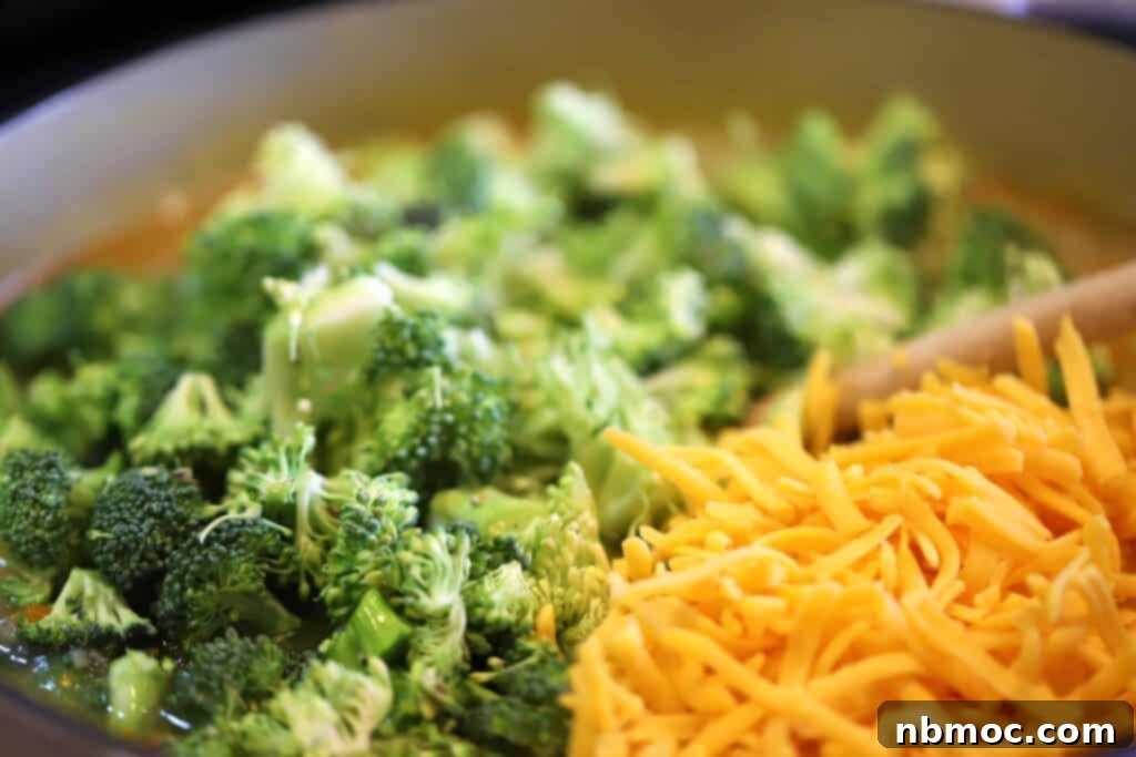 A vibrant selection of fresh ingredients laid out for Potato Broccoli Cheese Soup, including bright green broccoli florets, hearty potatoes, crisp carrots, fragrant onions, garlic cloves, and a block of cheddar cheese.