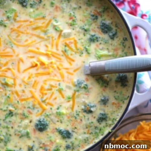 Broccoli Potato Soup simmering in a large Dutch oven, with a side bowl of shredded cheese and a serving spoon, inviting you to enjoy this comforting dish.