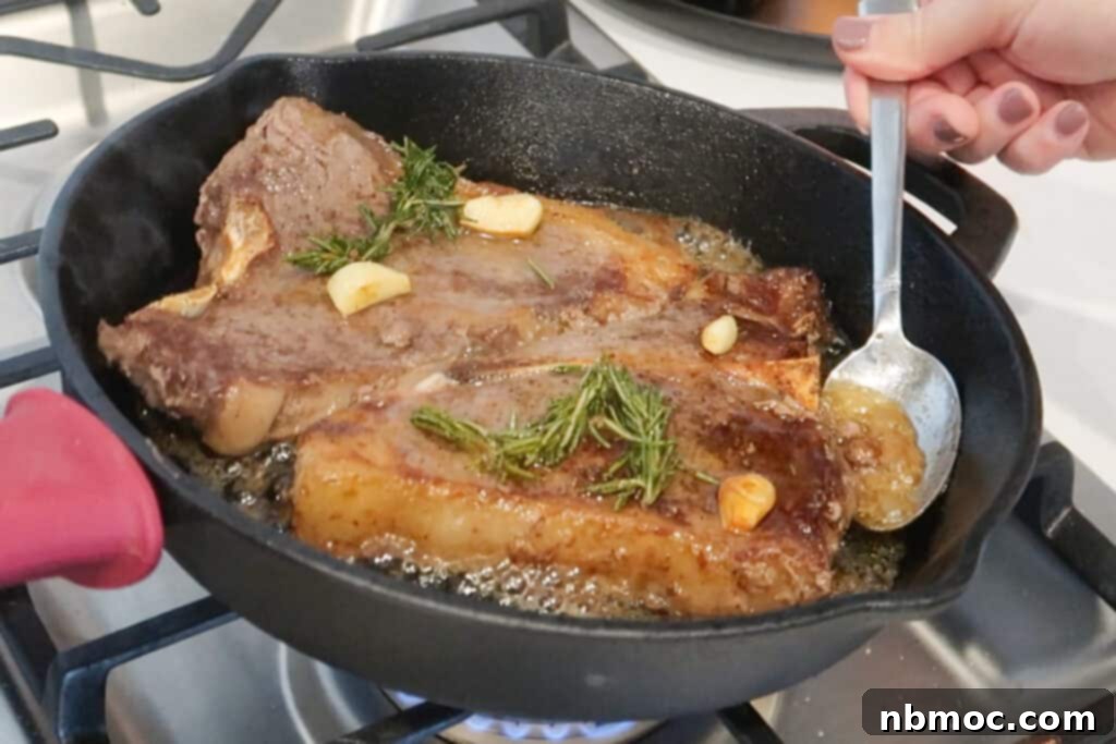 Stovetop steak recipe cooking in a cast-iron skillet with a hand basting them using a spoon, showing the technique for how to sear a steak in a pan.
