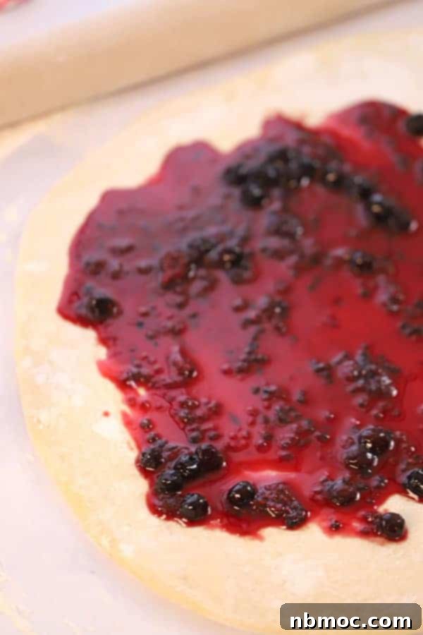 Sweet roll dough rolled out, covered in berry compote, and ready to be sliced.