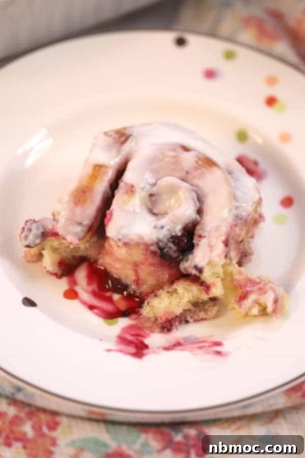 A single berry sweet roll on a plate, topped with generous lemon icing.
