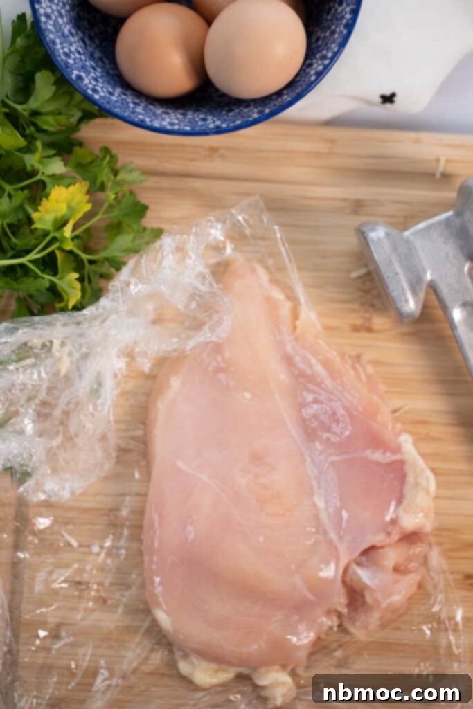 A cutting board with raw chicken breast being pounded.