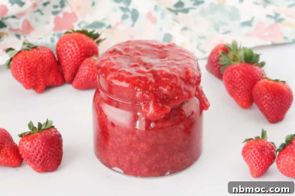 A glass jar overflowing with strawberry compote on a table surrounded by fresh strawberries, strawberry sauce recipes.