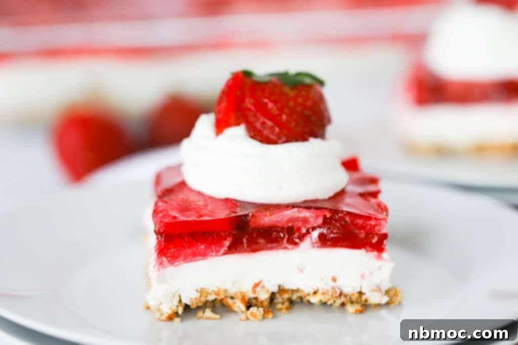 A delectable slice of classic strawberry pretzel salad, perfectly arranged on a plate and adorned with a generous swirl of whipped cream and fresh, juicy strawberries.