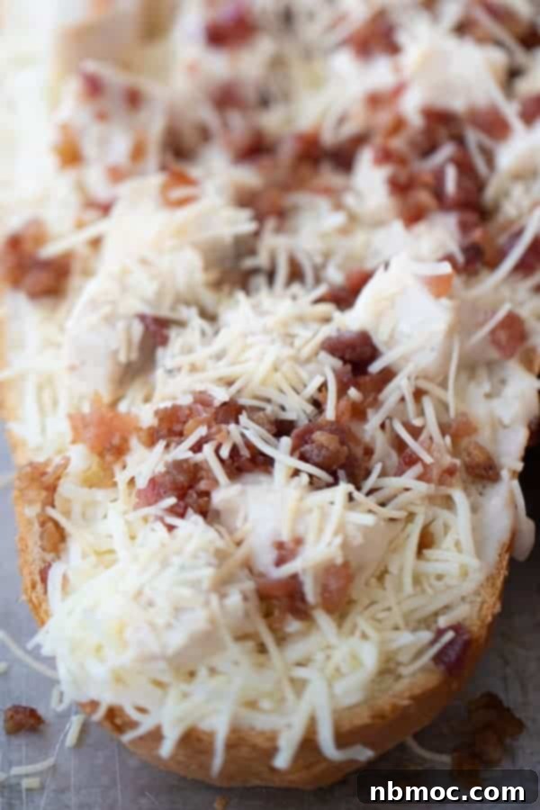Effortless French Bread Pizza 3 A loaf of french bread cut in half and topped with cheese, bacon and chicken, ready to be cooked in the oven.