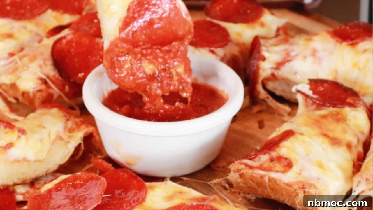 Effortless French Bread Pizza 5 A slice of pepperoni pizza bread being dipped into marinara sauce.