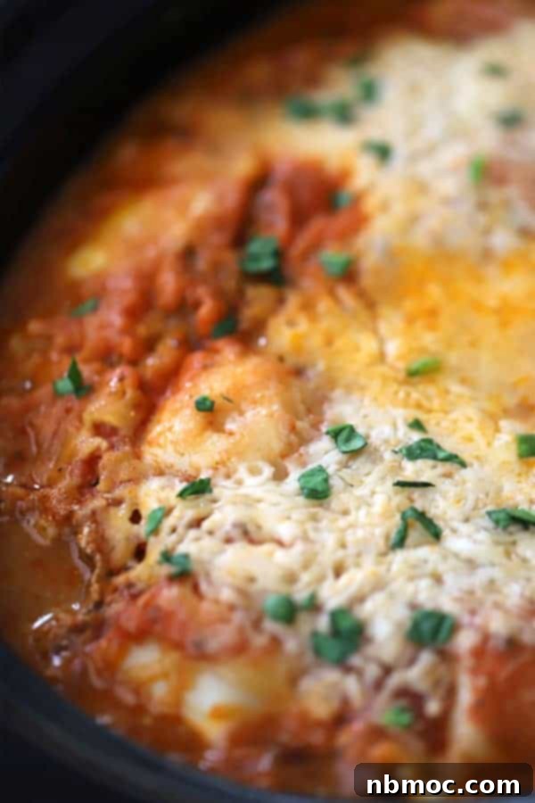 Effortless Slow Cooker Ravioli Lasagna 2 A crockpot with freshly cooked crockpot lasagna with ravioli, garnished with fresh herbs.