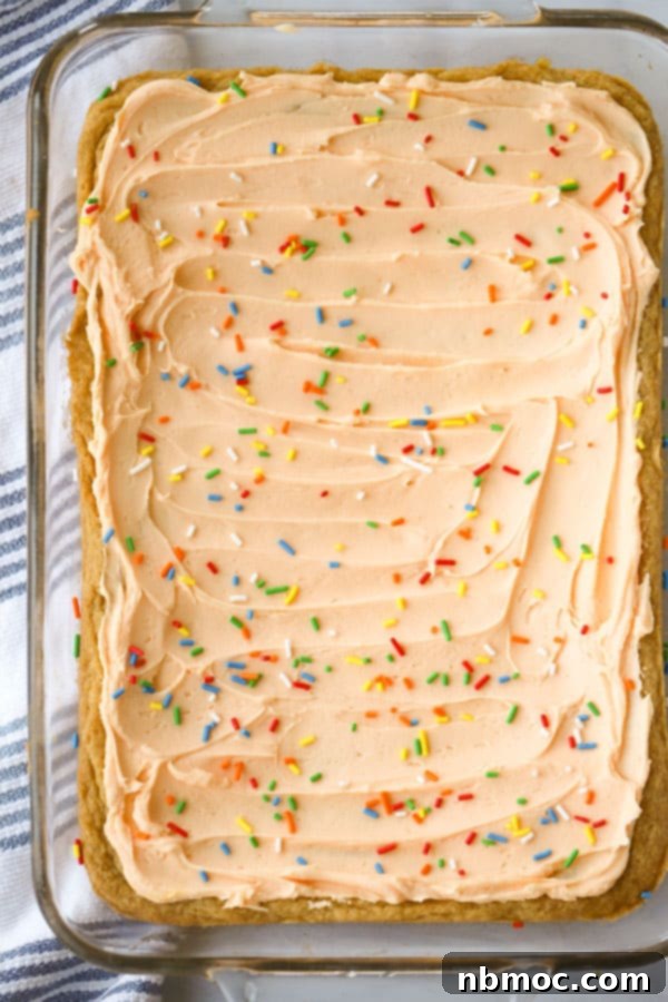 Sunshine Creamsicle Cookie Bars 3 A large baking dish filled with baked orange creamsicle bars, generously topped with a vibrant orange frosting and a scattering of colorful sprinkles, ready for slicing.