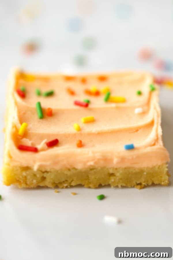 Sunshine Creamsicle Cookie Bars 4 Close-up of vibrant orange sugar cookies cut into perfect squares, topped with a generous swirl of creamy orange frosting and decorative sprinkles, showcasing their appealing texture.