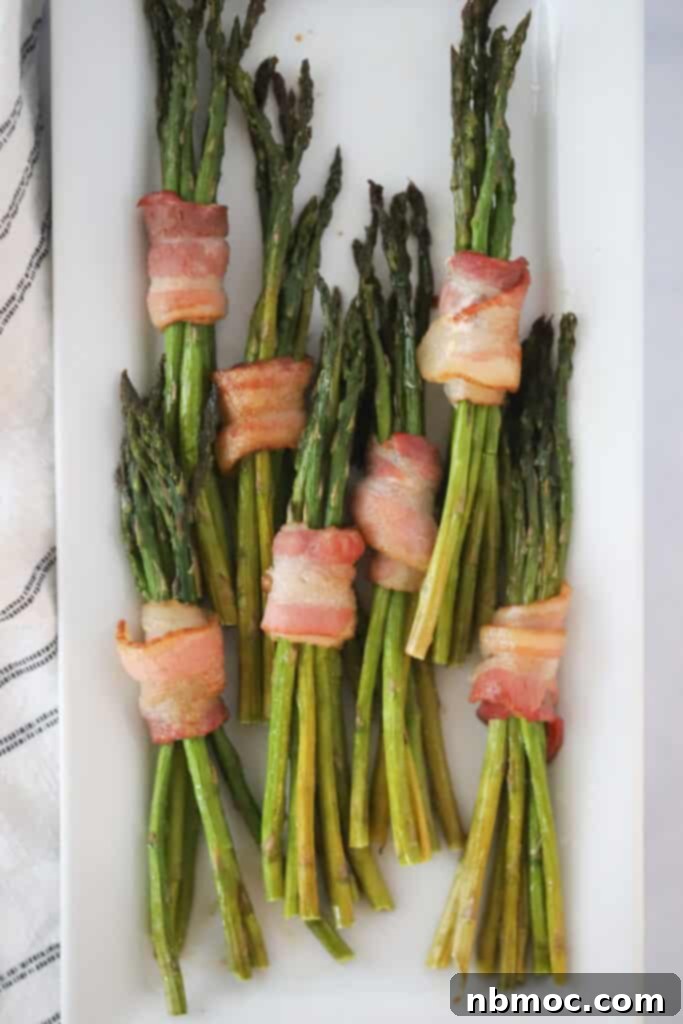 Perfectly cooked air fryer bacon wrapped asparagus spears arranged on a white serving plate, a unique and savory brunch idea.