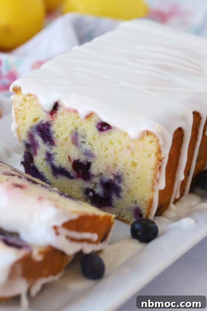 A loaf of lemon blueberry bread, topped with a lemon glaze, a perfect quick bread for brunch.
