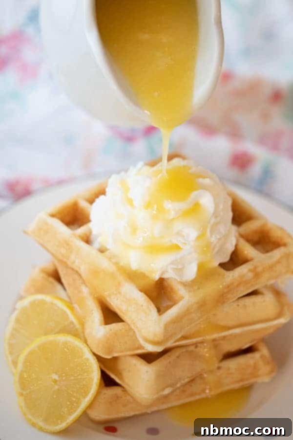 Lemon syrup being poured over fluffy waffles with whipped cream, a bright and zesty topping.