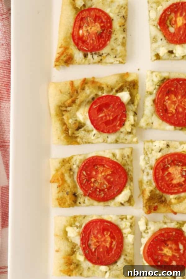 Three cheese flatbread, sliced into rectangles and garnished with tomatoes and herbs, a perfect appetizer.