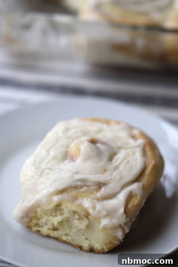 Pillowy, warm homemade cinnamon rolls drizzled with cream cheese icing, served on a white plate, perfect for Sunday brunch.