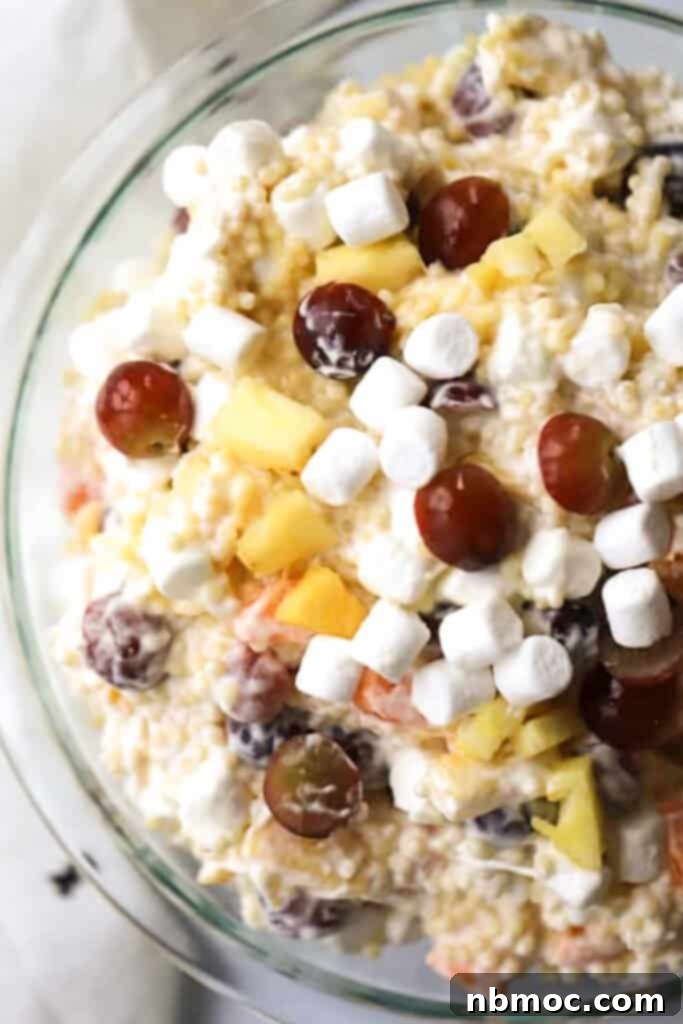 A beautifully presented bowl of creamy Frog Eye Salad, garnished with fresh grapes and mini marshmallows, ready to be served at a potluck or BBQ.