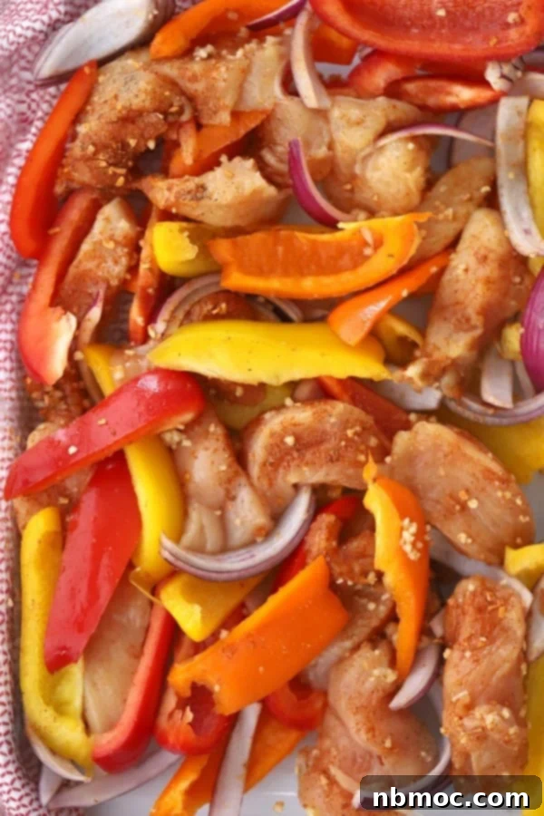 A vibrant sheet tray filled with seasoned sliced chicken, colorful bell peppers (red, orange, yellow), and onions, ready for baking into delicious chicken fajitas.