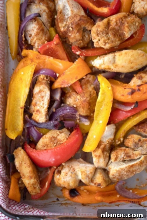 Close-up of golden-brown baked sheet pan chicken fajitas with a colorful mix of red, orange, and yellow bell peppers and onions.