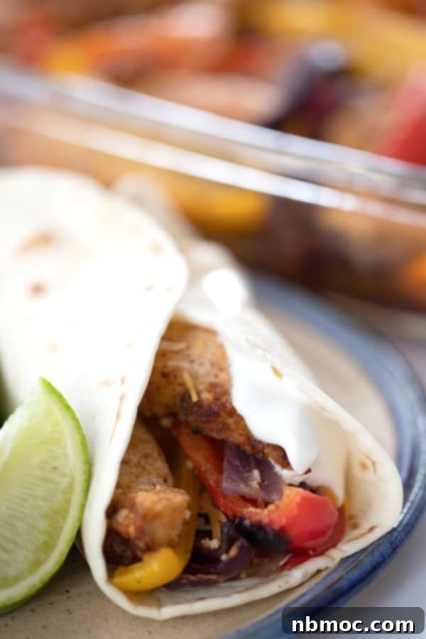 A plate holding a warm tortilla generously filled with oven-baked chicken fajitas, topped with sour cream and cilantro, ready to be enjoyed.