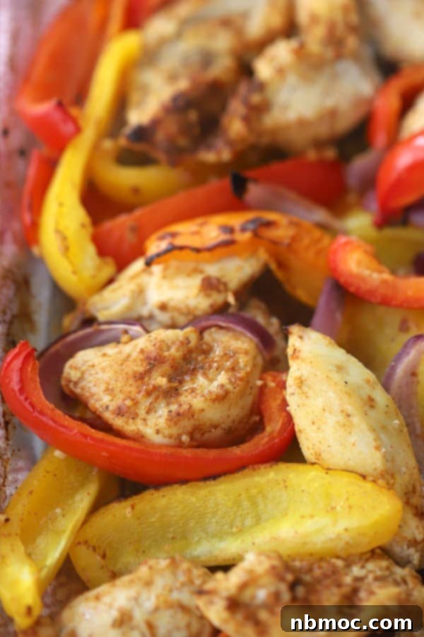 Close-up of seasoned chicken and colorful bell peppers spread on a baking sheet, glistening and ready for the oven to become delicious baked fajitas.