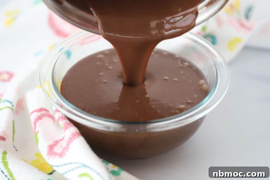 Smooth homemade chocolate pudding being poured into a clear glass bowl, showcasing its rich, glossy texture, perfect for an easy chocolate pudding recipe.