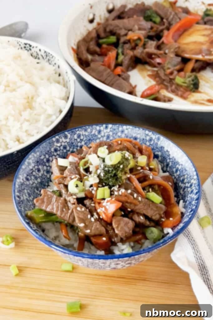 Decorative serving bowls full of rice and Korean Beef Stir Fry on a countertop, garnished with green onions and sesame seeds.