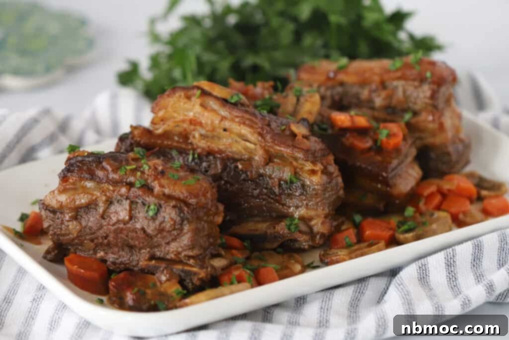 A white serving platter full of Slow Cooker Beef Ribs and veggies. The best beef short ribs slow cooker recipe.