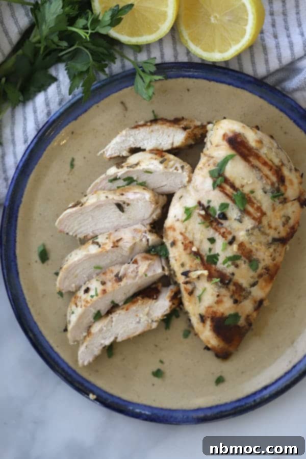 Flavorful Rosemary Garlic Chicken Breast Marinade 5 A plate featuring two perfectly grilled chicken breasts, marinated with rosemary and garlic, garnished with fresh herbs.